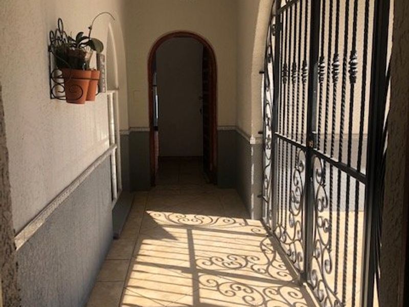 A covered entrance hallway featuring tiled flooring, an arched doorway, and a decorative wrought iron security gate.