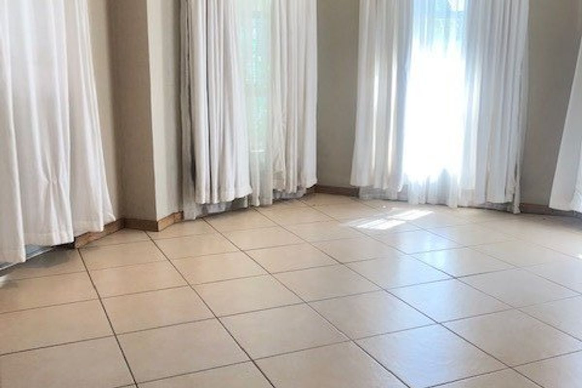 A bright, empty living area featuring neutral ceramic floor tiles and large windows with floor-to-ceiling curtains.