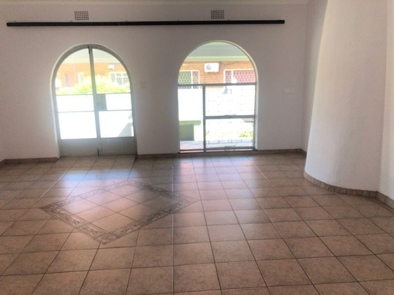 Spacious living area featuring ceramic tile flooring with decorative inlay, arched glass doors providing natural light, and a unique curved wall architectural detail.