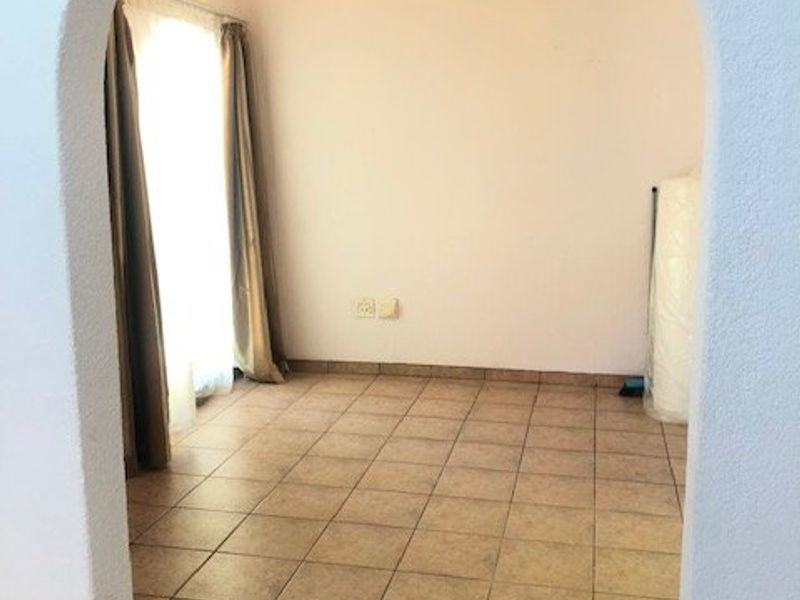 An empty living room featuring an arched entryway, ceramic tiled flooring, and a decorative chandelier.