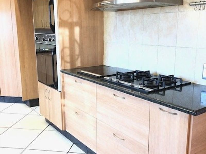 A functional kitchen featuring light wood cabinetry, granite countertops, a built-in oven, and a gas hob with a stainless steel extractor fan.