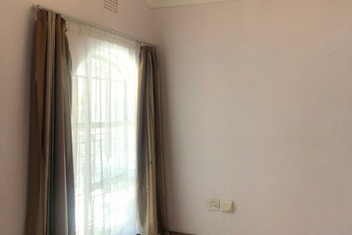 An empty bedroom featuring tiled flooring, a vaulted ceiling with decorative cornice, and an arched window with security bars.