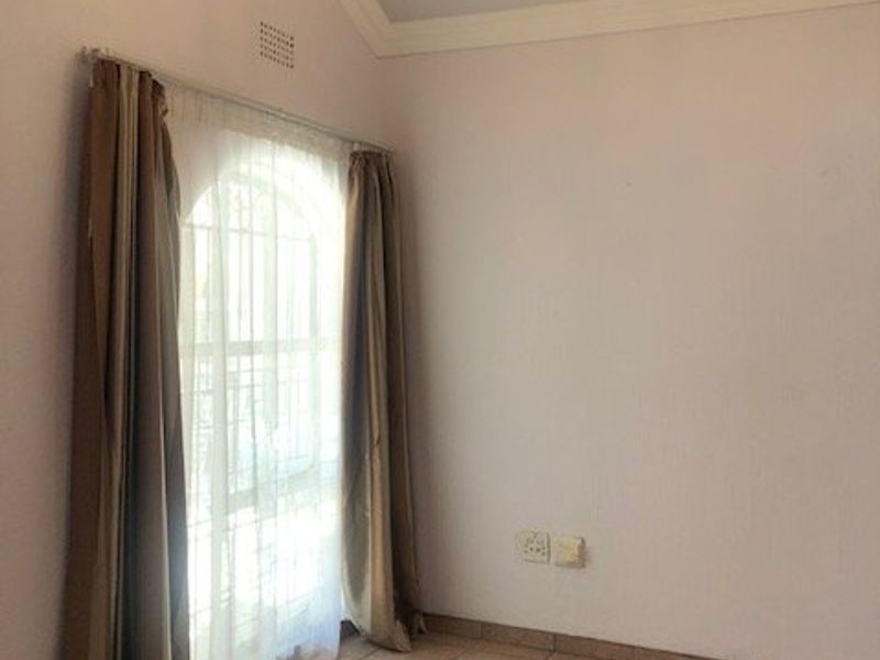 An empty bedroom featuring tiled flooring, a vaulted ceiling with decorative cornice, and an arched window with security bars.
