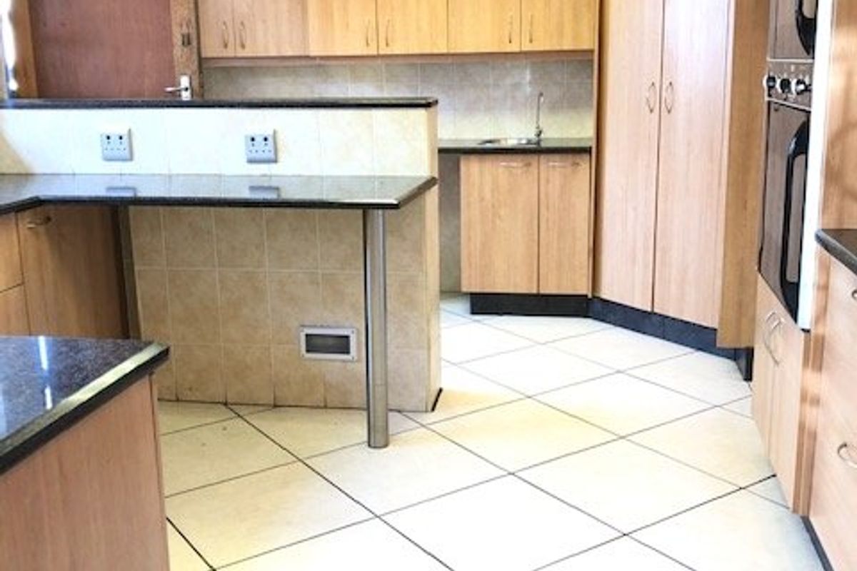 A spacious kitchen featuring light wood cabinetry, granite countertops, a breakfast bar, and a built-in double oven with tiled flooring throughout.