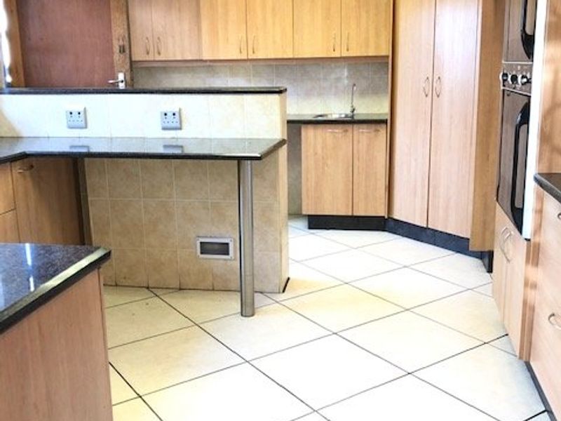 A spacious kitchen featuring light wood cabinetry, granite countertops, a breakfast bar, and a built-in double oven with tiled flooring throughout.