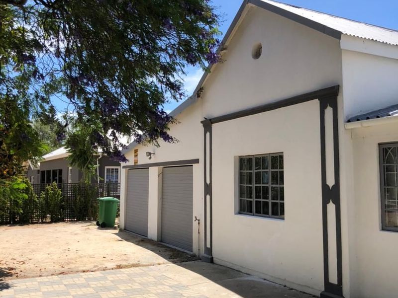 Front exterior view of the property featuring a double garage, paved driveway, and well-maintained white facade with dark trim detailing.