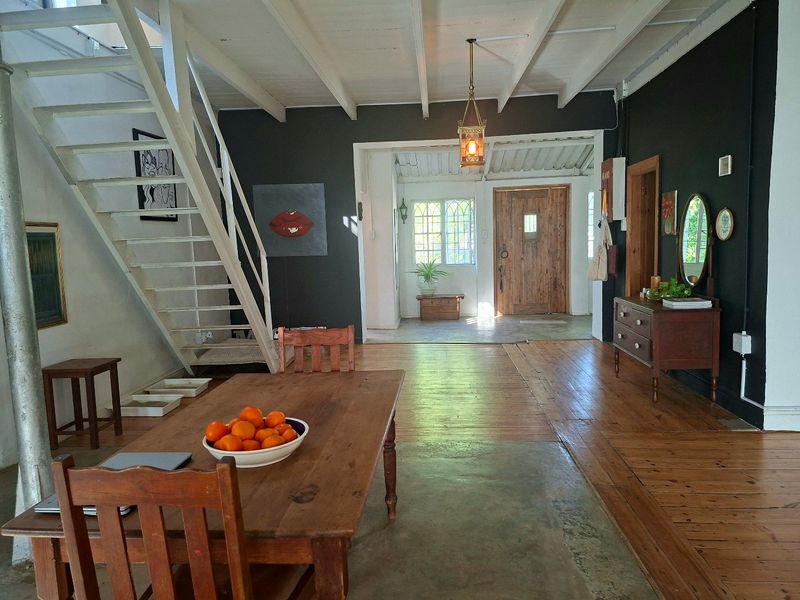Spacious living area featuring exposed beam ceilings, a mix of hardwood and concrete flooring, and a characterful timber staircase leading to the upper level.