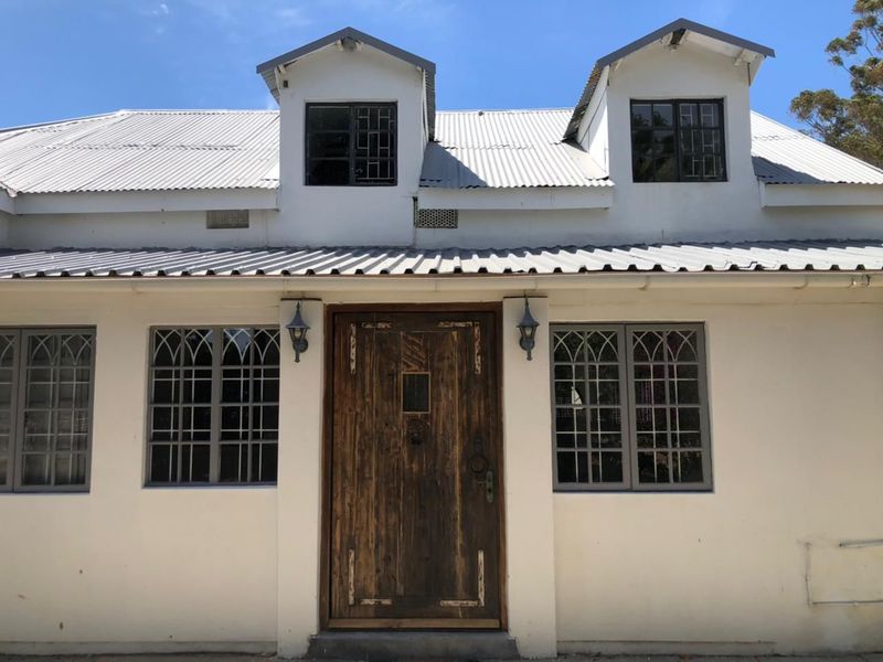 Front facade of a cottage-style home featuring a corrugated metal roof, dormer windows, and a rustic timber entrance door.