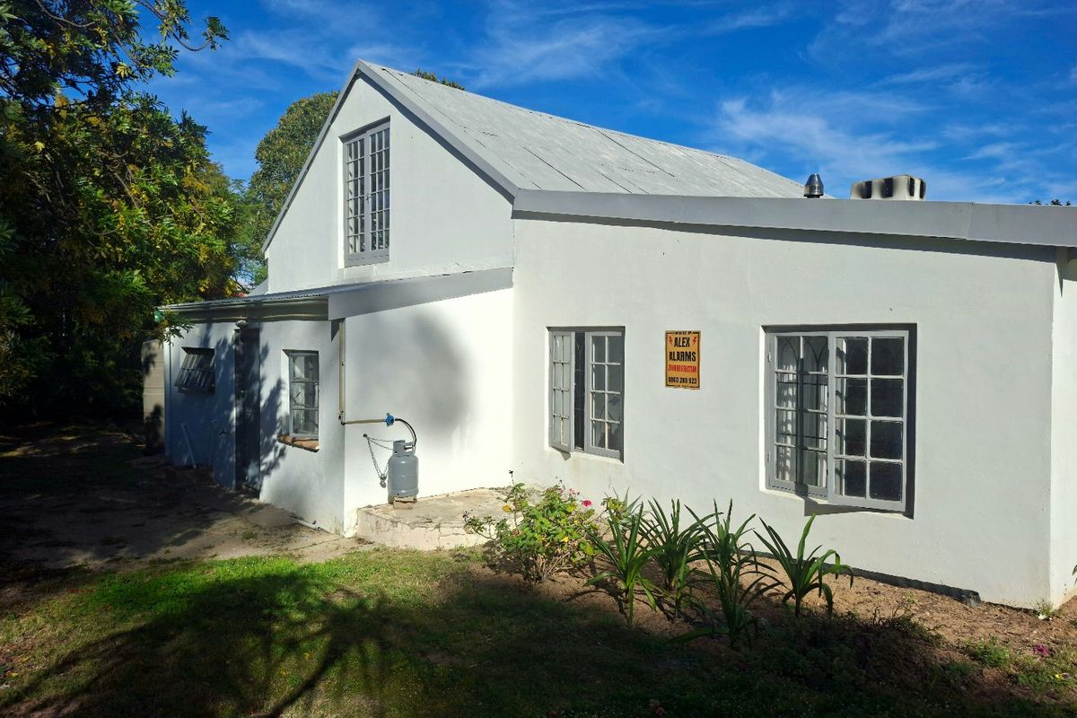 Rear exterior view of the house featuring a pitched metal roof, casement windows, and a small garden area.