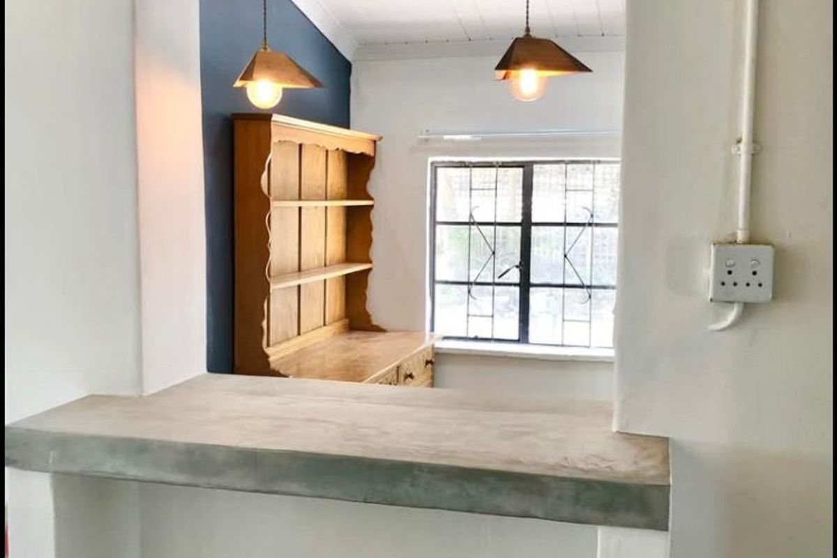 A kitchen view featuring a concrete breakfast bar, pendant lighting, and a timber-accented ceiling, creating a rustic yet functional preparation and dining space.