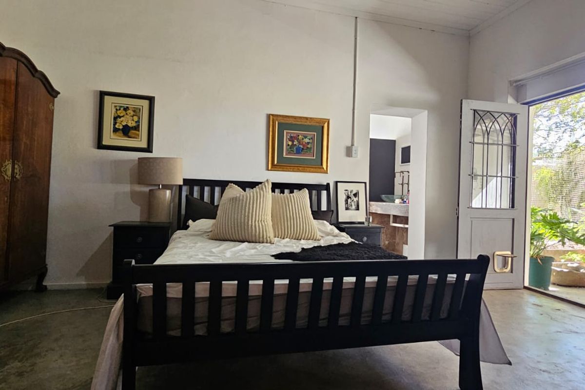 Spacious bedroom featuring concrete flooring, exposed beam ceilings, and direct access to an outdoor patio area through a glass-paneled door.