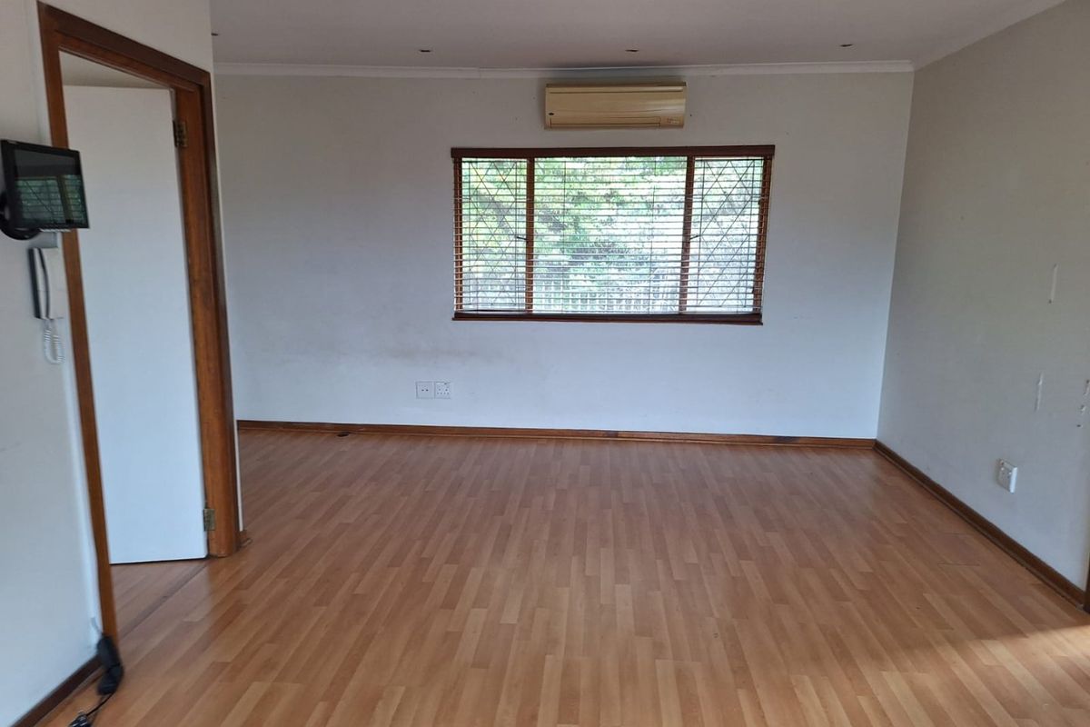 An empty living room featuring laminate flooring, recessed lighting, and a wall-mounted air conditioning unit, providing a blank canvas for personalization.