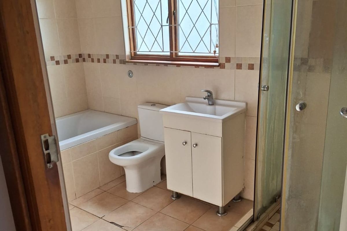 A functional bathroom featuring a built-in bathtub, separate shower enclosure, vanity cabinet, and toilet, finished with neutral wall and floor tiling.