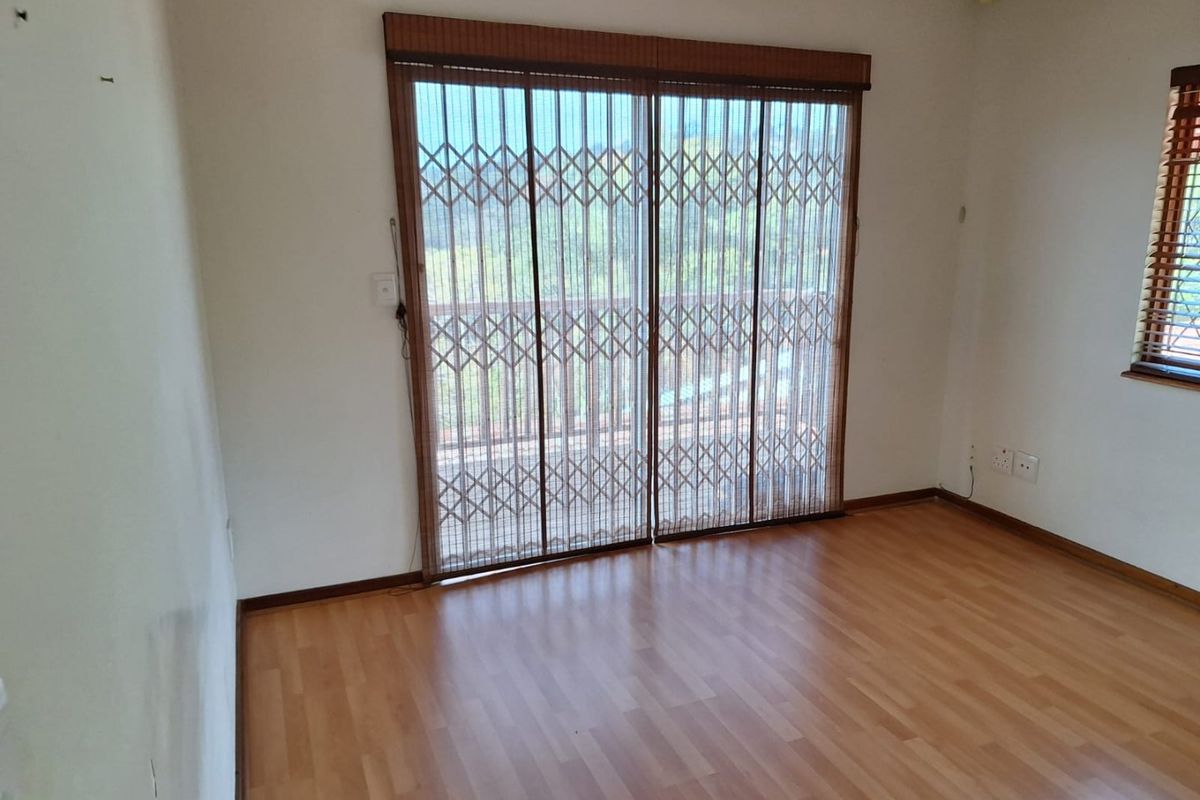 An empty bedroom featuring laminate flooring, timber blinds, and a sliding glass door with an integrated security gate leading to an outdoor area.