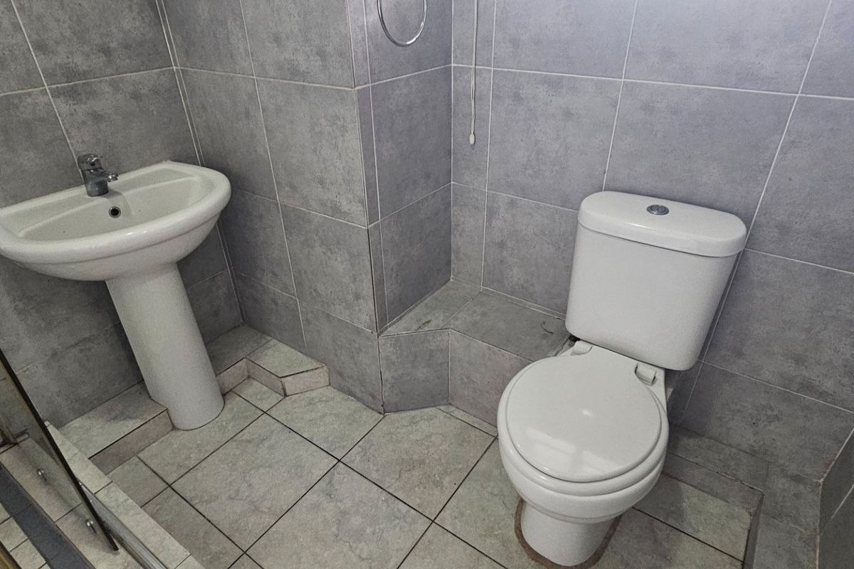 A clean, modern bathroom featuring grey ceramic wall and floor tiles, a pedestal washbasin, and a dual-flush toilet.