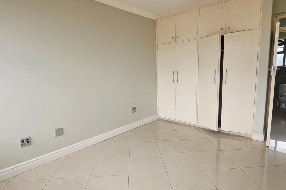 An empty bedroom featuring tiled flooring, built-in cupboards, and direct access to an en-suite bathroom.