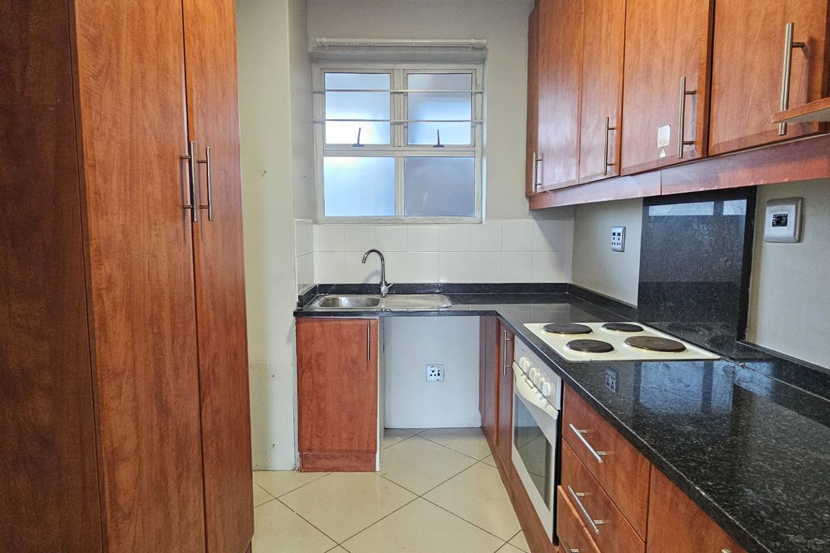 A functional kitchen featuring wood-finish cabinetry, granite countertops, a built-in oven and hob, and tiled flooring.