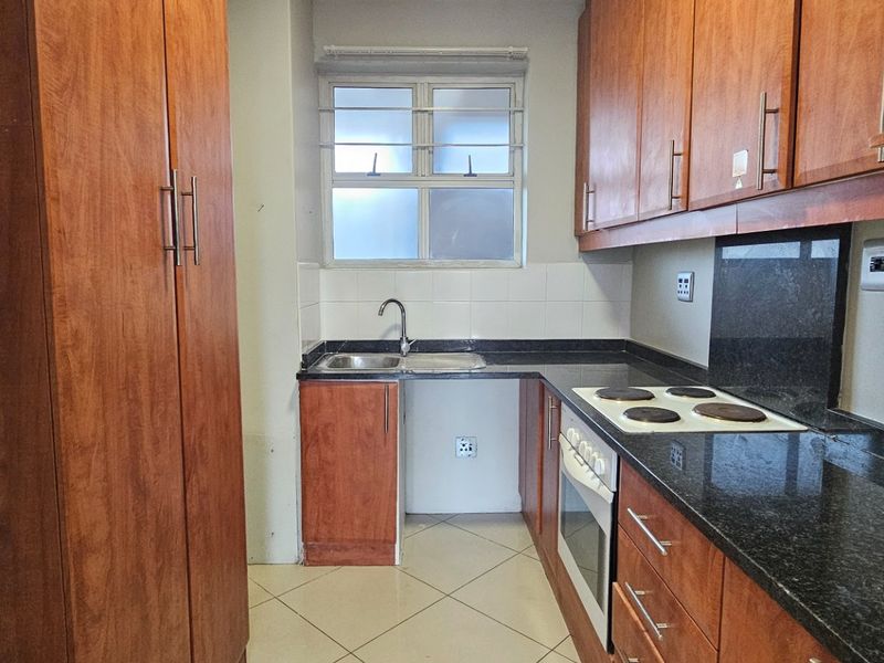 A functional kitchen featuring wood-finish cabinetry, granite countertops, a built-in oven and hob, and tiled flooring.