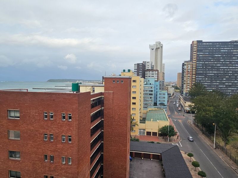 Elevated urban and coastal view overlooking surrounding apartment buildings, city streets, and the nearby beach coastline.