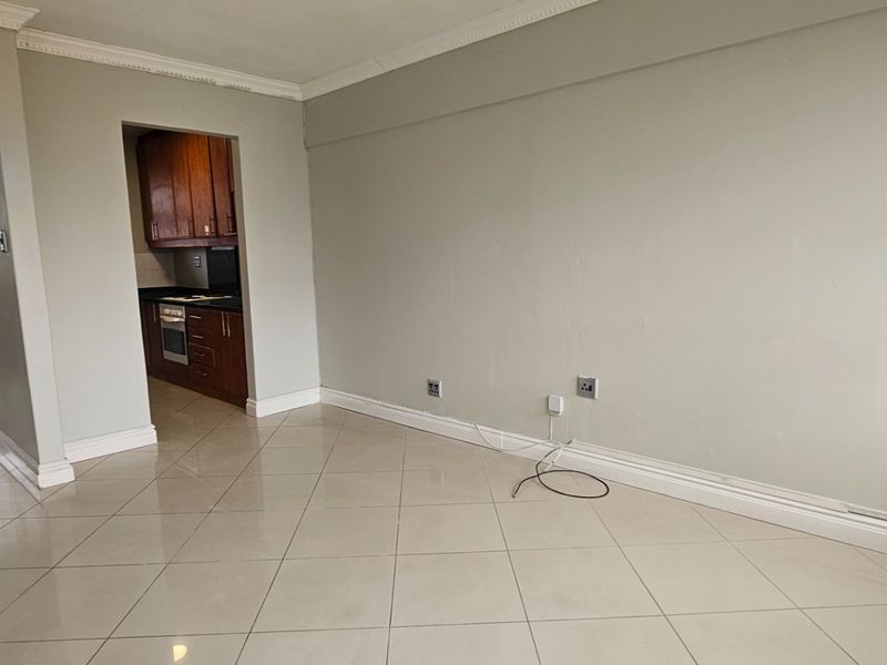 A bright, empty living area featuring neutral tiled floors, crown molding, and a direct view into the adjacent kitchen space.