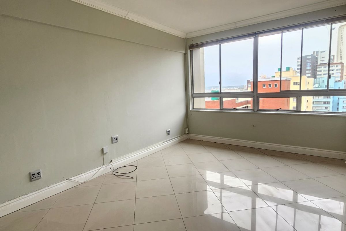 A bright, empty living area featuring tiled floors, crown molding, and large windows offering an urban view, ready for personalization.