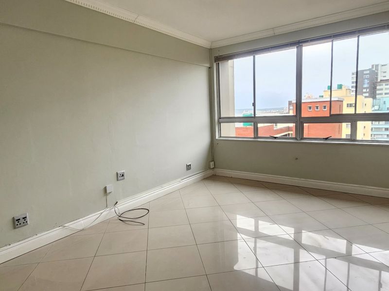 A bright, empty living area featuring tiled floors, crown molding, and large windows offering an urban view, ready for personalization.
