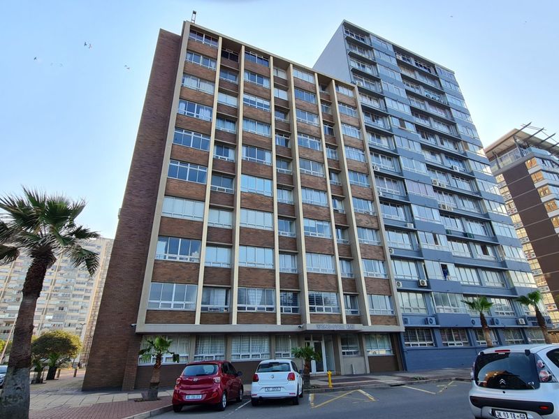 A multi-story apartment building facade featuring brick and concrete construction with large windows, situated in an urban street setting.