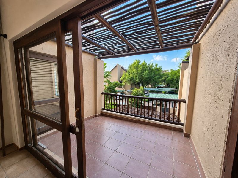 A covered balcony featuring tiled flooring, a wooden pergola structure, and a wooden railing, offering an open outdoor space accessible via sliding glass doors.