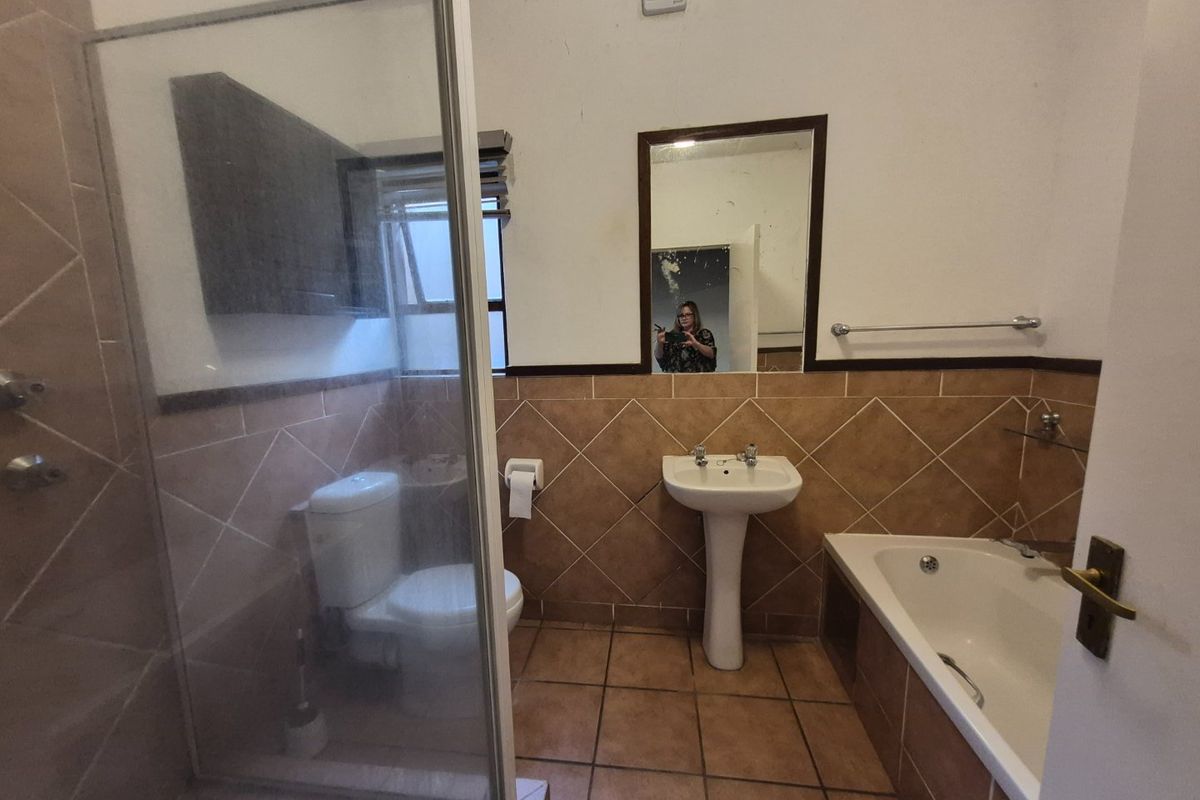 A dated bathroom featuring a pedestal basin, shower enclosure, and built-in bathtub with tiled finishes, requiring cosmetic updates to modernize the space.