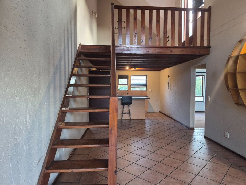Open plan living area featuring a wooden staircase leading to a mezzanine loft, tiled flooring, and a functional kitchen area.