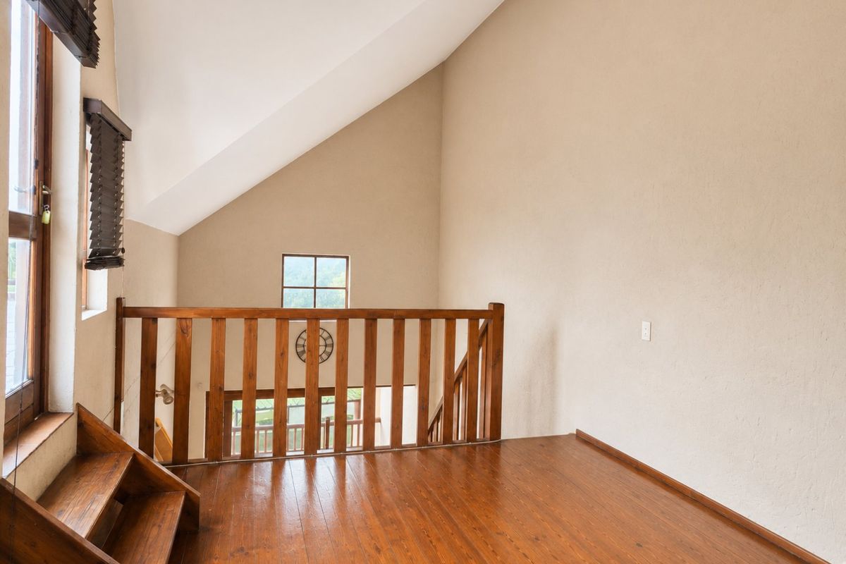 A bright loft-style bedroom featuring vaulted ceilings, timber flooring, and a wooden balustrade overlooking the lower level.