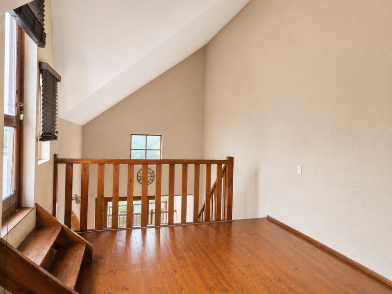 A bright loft-style bedroom featuring vaulted ceilings, timber flooring, and a wooden balustrade overlooking the lower level.
