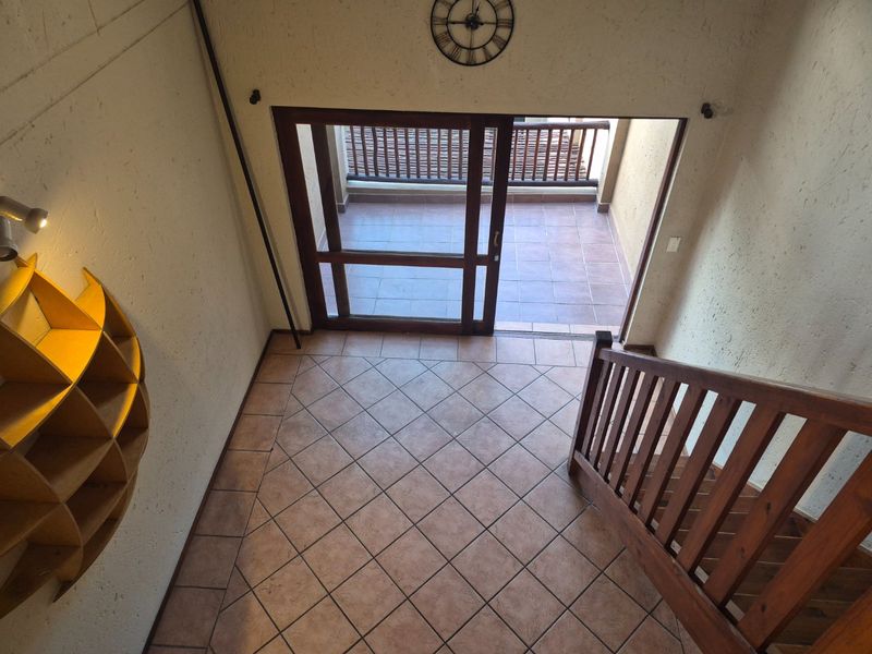 An entrance area featuring tiled flooring, a wooden staircase with a matching balustrade, and a sliding glass door leading out to a balcony.