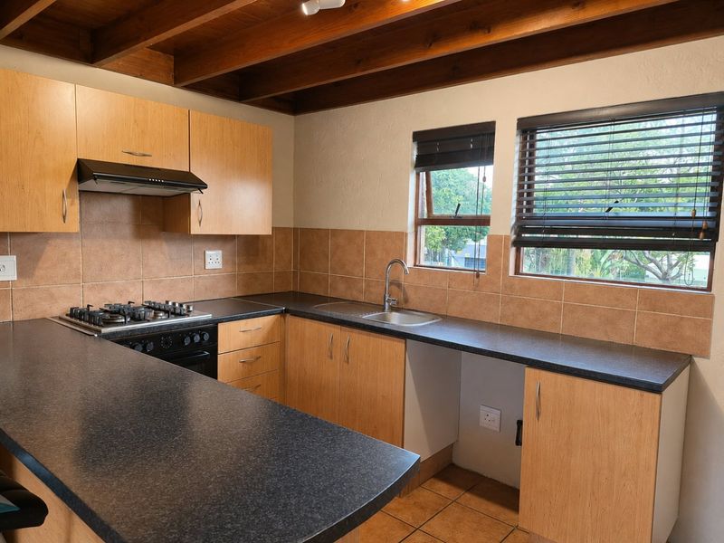 A functional kitchen featuring light wood cabinetry, dark laminate countertops, a gas hob with extractor, and exposed timber ceiling beams.