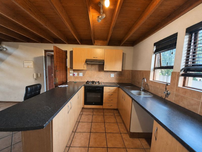 A functional kitchen featuring wooden cabinetry, dark laminate countertops, a gas hob, built-in oven, and exposed timber ceiling beams.