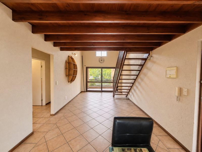 Spacious living area featuring exposed timber ceiling beams, tiled flooring, and a timber staircase leading to an upper level with balcony access.