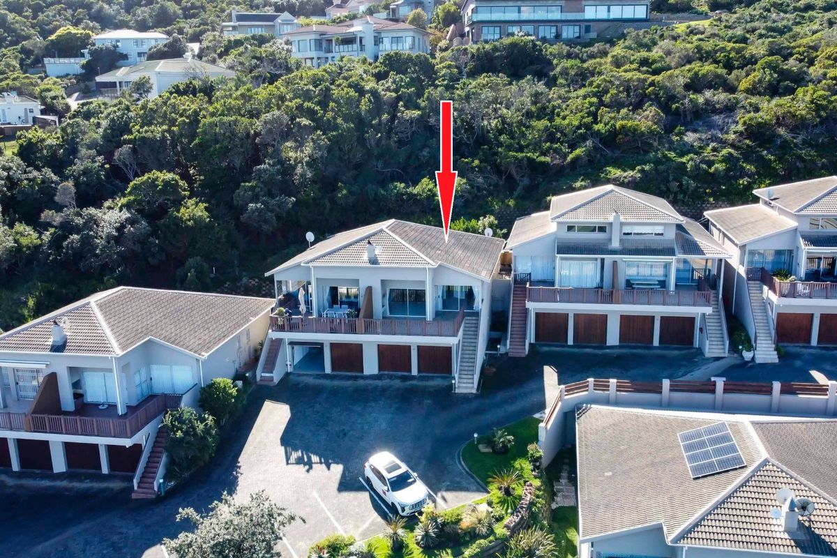 Aerial view of a multi-level townhouse complex featuring tiled roofs, balconies, and integrated garages set against a hillside landscape.