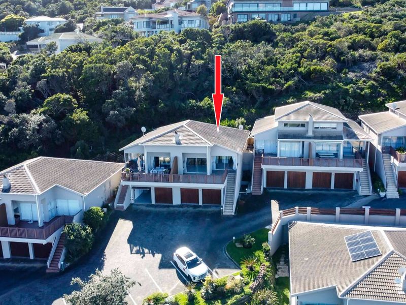 Aerial view of a multi-level townhouse complex featuring tiled roofs, balconies, and integrated garages set against a hillside landscape.