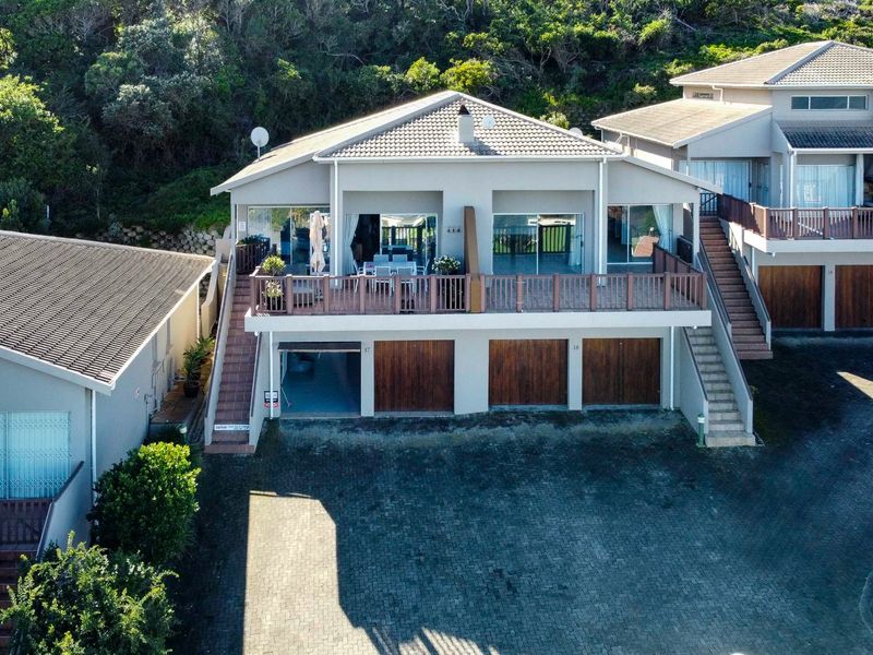 Aerial view of a townhouse complex featuring a paved driveway, multiple wooden garage doors, and elevated timber decks with sliding glass door access.