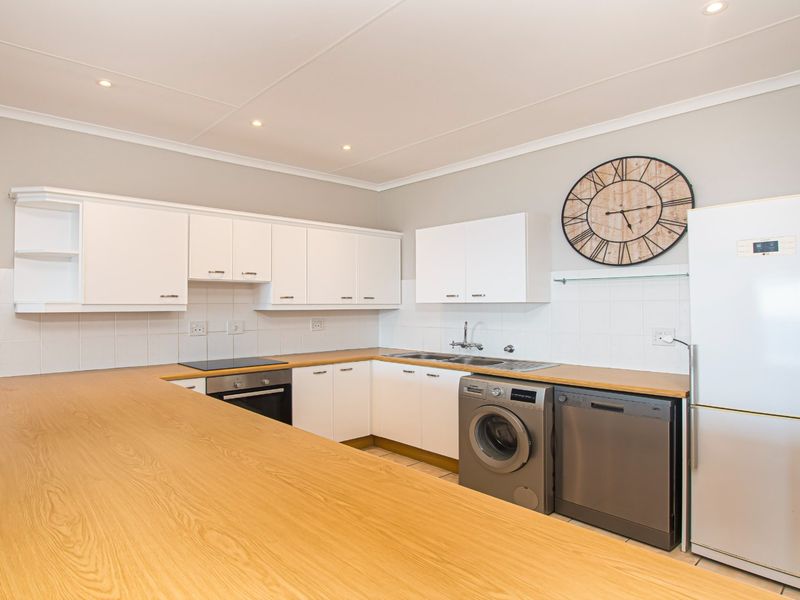 A functional kitchen featuring white cabinetry, wooden countertops, a built-in oven, electric hob, and tiled backsplash with integrated space for appliances.