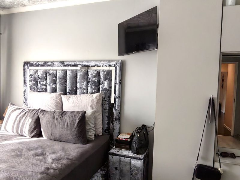 A well-maintained bedroom featuring built-in cupboards with mirrored doors and a wall-mounted television bracket, offering functional storage and layout.