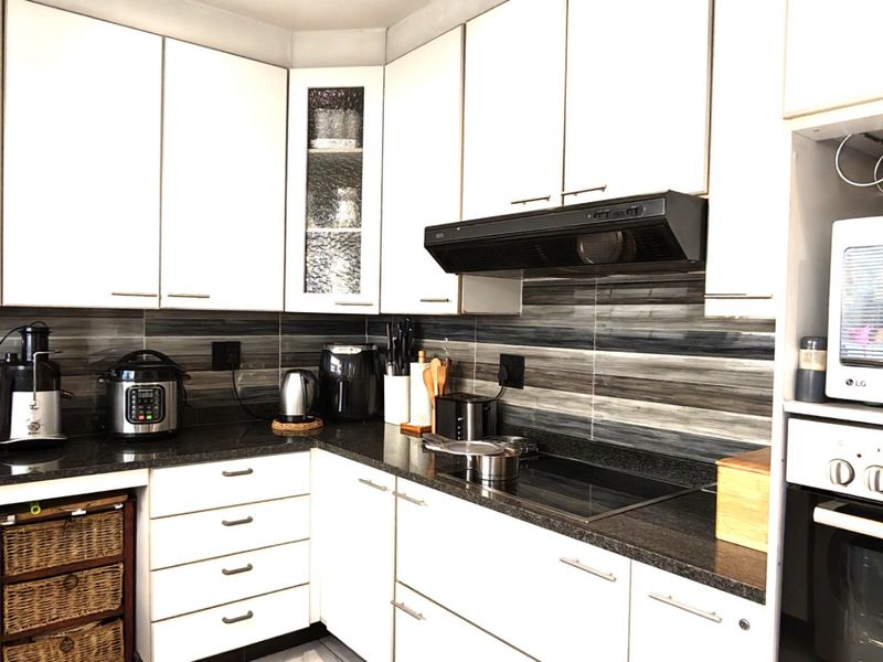 A functional kitchen featuring white cabinetry, dark granite countertops, a tiled backsplash, and integrated appliances including an oven and extractor fan.