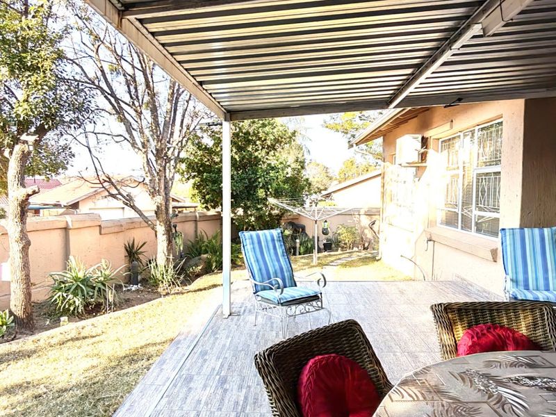 A covered outdoor patio area featuring tiled flooring and a corrugated metal roof, overlooking a private garden space with perimeter walling.