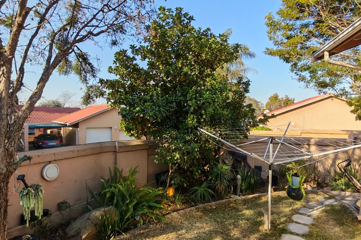A rear exterior view of the townhouse featuring a garden area, perimeter wall, and security bars on the windows.