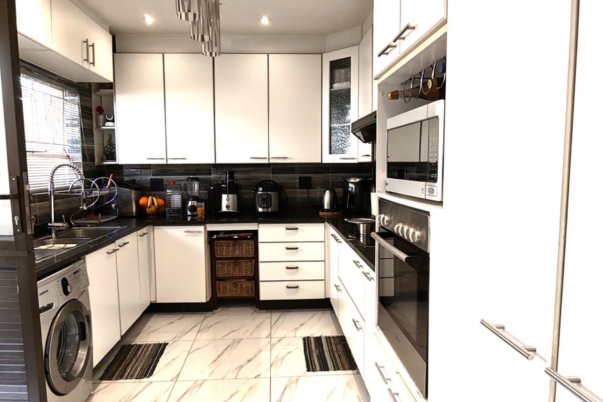 A modern, well-appointed kitchen featuring white cabinetry, integrated appliances, a tiled backsplash, and marble-look floor tiles, offering a clean and functional workspace.