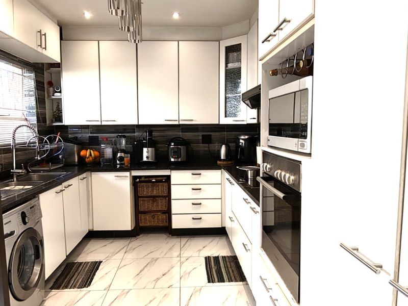 A modern, well-appointed kitchen featuring white cabinetry, integrated appliances, a tiled backsplash, and marble-look floor tiles, offering a clean and functional workspace.