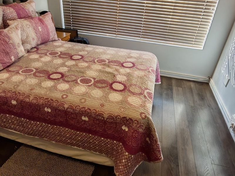 A well-maintained bedroom featuring dark laminate flooring and adjustable venetian blinds, providing a clean and functional living space.