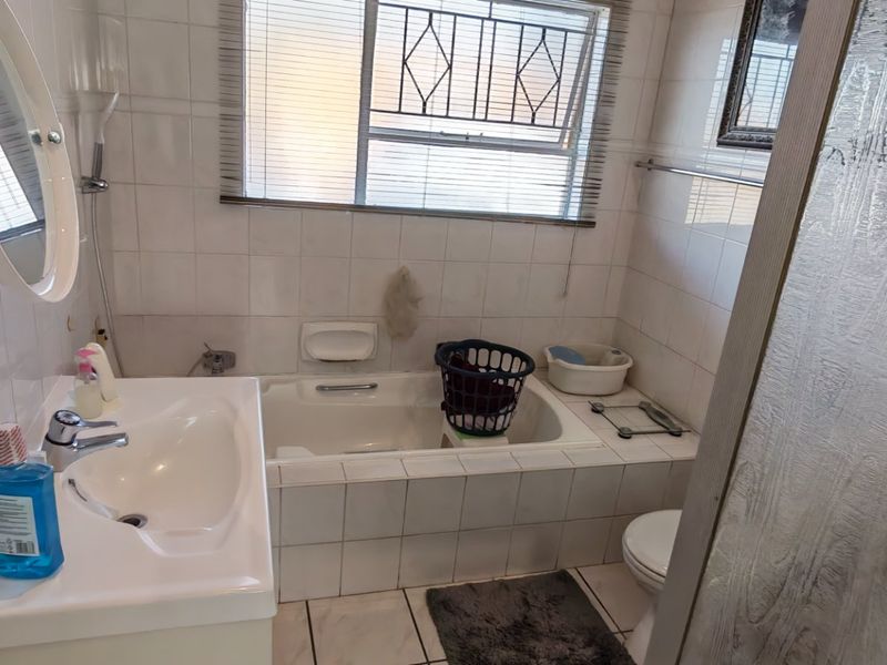 A functional bathroom featuring a built-in bathtub, vanity basin, and tiled finishes, offering a practical layout with potential for modern cosmetic updates.