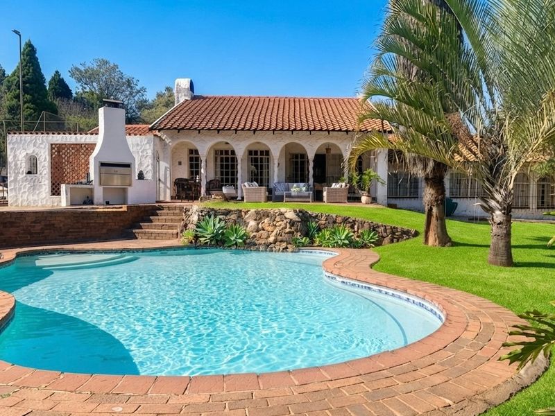 A well-maintained outdoor area featuring a swimming pool with brick coping, a stone retaining wall, and a covered patio with a built-in fireplace.