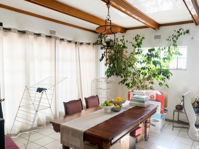 A dining room featuring exposed timber ceiling beams, ceramic floor tiles, and a central pendant light fixture.